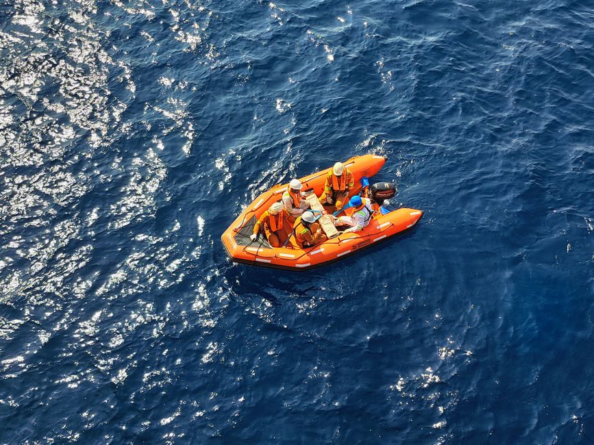 An aerial view of a group in an orange inflatable raft navigating the deep blue ocean waters.